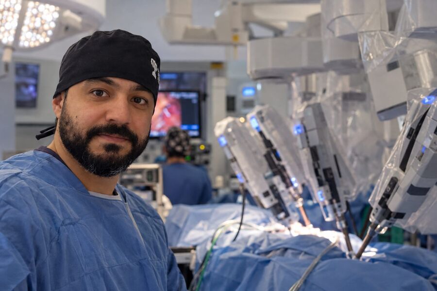 Dr. Alzemir Santos em sala cirúrgica, com os braços da plataforma robótica ao fundo